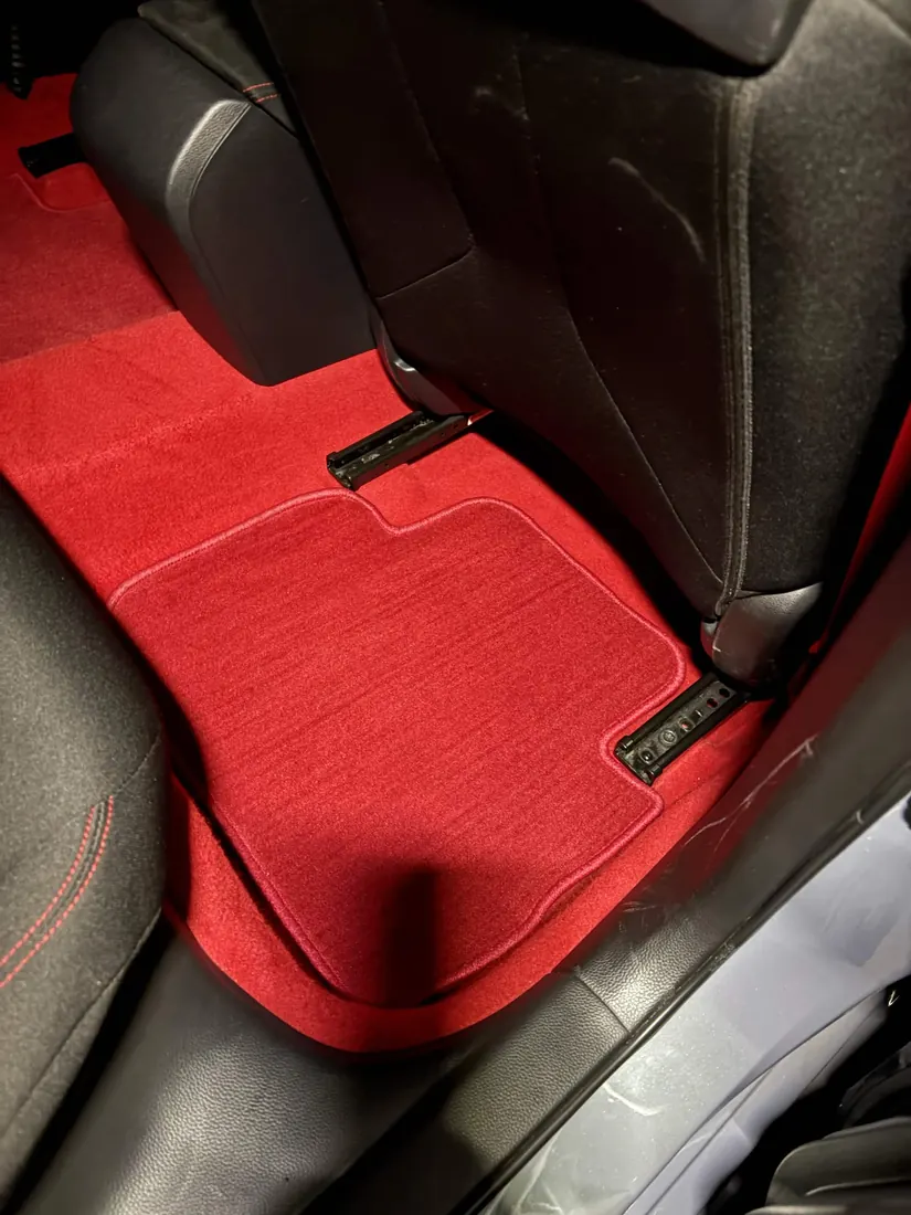 Red carpet floor mat in the rear footwell, freshly vacuumed